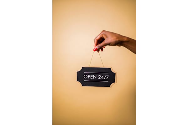 A hand is holding a sign that says "OPEN 24/7".
